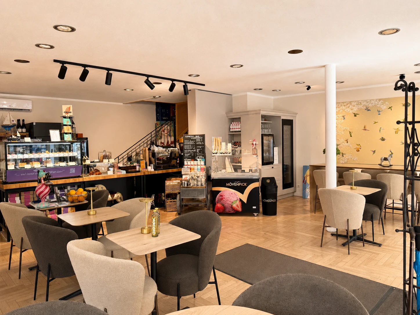 Heller Cafébereich mit Tischen, Sesseln und Verkaufstheke